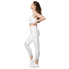 A full-length side view of a white-skinned girl shows her beautiful white light-patterned yoga pants. The garment features a double-layered, crossover waist design, and the photo is against a white background. Her hands are on her hips, and the image is cropped from her stomach. She also wears white tennis shoes and white athletic pants.