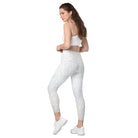 A full-length side view of a white-skinned girl shows her beautiful white light-patterned yoga pants. The garment features a double-layered, crossover waist design, and the photo is against a white background. Her hands are on her hips, and the image is cropped from her stomach. She also wears white tennis shoes and white athletic pants.