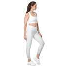 A full-length side view of a white-skinned girl shows her beautiful white light-patterned yoga pants. The garment features a double-layered, crossover waist design, and the photo is against a white background. Her hands are on her hips, and the image is cropped from her stomach. She also wears white tennis shoes and white athletic pants.