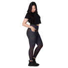 An Asian girl wearing Salt Skins Black Workout Leggings with Pockets, a black top, and black tennis shoes is seen posing against a white background, revealing her yoga pants from the side. There are delicate color patterns on the performance fabric.