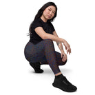 An Asian girl wearing Salt Skins Black Workout Leggings with Pockets, a black top, and black tennis shoes is kneeling and posing against a white background, exposing the back of her yoga pants. There are delicate color patterns on the performance fabric.