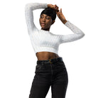 A dark-skinned girl wearing a cropped, long-sleeved workout top with a white light pattern is standing against a white wall. She is wearing jeans and white shoes. She has her hands together on top of her head, showcasing the front of her yoga top. The jeans and white shoes are against a white wall, showing the front of her yoga top. A model wearing clothing has her hands on the top of her head.