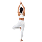 This full-length image features a girl wearing pretty white yoga leggings with subtle check patterns on the back. The leggings have a double-layered waist. The black-haired woman is doing yoga, her hands clasped together, pointing up over her head.