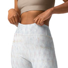 A close-up of a girl wearing a tan workout bra while holding the waist of her yoga pants. She is wearing lovely white yoga leggings (shown from the front) with a double-layered waist and the white leggings have subtle check patterns. The image is cropped and you can only see her athletic pants from the things up to her workout bra.