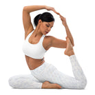 This full-length image features a girl wearing pretty white yoga leggings with subtle check patterns. The leggings have a double-layered waist. The black-haired woman is doing yoga, her hands clasped together, pointing up over her head in a yoga pose with her feet touching her hands in a v-pose.