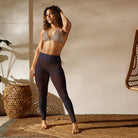 Girl standing on a tan wicker mat, wearing a tan swimsuit top, with her hand in her hair wearing Salt Skins Flat Front Yoga Workout Pants with a subtle multicolor fleck of purple and red color pattern.