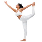 This image features a full-length side view of a girl wearing tight white yoga leggings that have a beautiful subtle check pattern in the performance fabric. The leggings include a double-layered waist. The black-haired woman is executing an extreme yoga pose, standing on one foot while holding her other foot behind her back with one arm while her other is pointing to the sky.